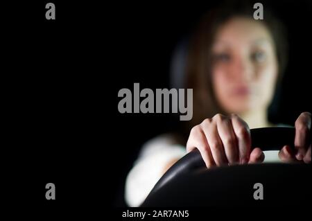 la jeune fille en arrière-plan dans la mise au point maintient le volant avec ses mains. Nuit, la fille dans la voiture est seule, seulement les mains et la direction wh Banque D'Images