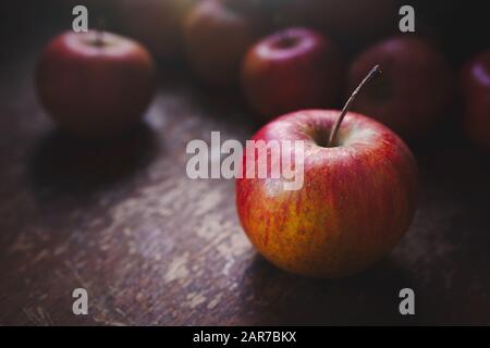 Pommes rouges, fraîches, brillantes, biologiques, cultivées, une à l'avant, sur une table et lumière venant de la fenêtre Banque D'Images