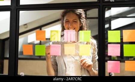 Un employé souriant d'une femme caucasienne développe une idée sur les notes collantes Banque D'Images