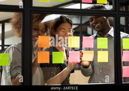 Des collègues multiraciaux souriants développent un projet sur des notes collantes Banque D'Images