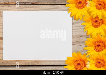 Une feuille de papier blanc entourée de tournesols sur un fond en bois. Banque D'Images