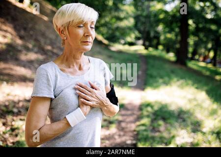 Senior woman avec douleur à la poitrine qui souffrent de crise cardiaque pendant le jogging Banque D'Images