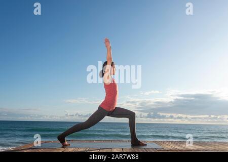 Femme sportive dans les vêtements de sport pratiquant le yoga, debout dans la pose d'anjaneyasana, emplacement idyllique près de l'océan Banque D'Images