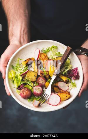 Salade de pommes de terre cuites au four et de légumes radiques dans les mains des hommes. Salade de légumes saine Banque D'Images