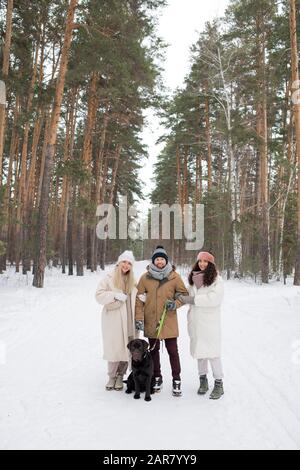 Jeune homme avec un retriever noir et deux filles en hiver debout sur la route Banque D'Images