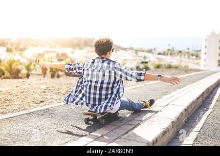 Garçon assis sur son skateboard bras ouverts, profitant d'une belle soirée à l'extérieur. Ado tendance s'amuser avec le skate, le panorama marin de la lumière du soleil Banque D'Images