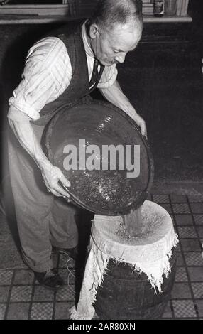 Années 1950, historique, faire de l'hydromel, un homme tenant un bol peu profond, versant du liquide, peut-être un mélange d'épices chauffées, dans un bol en grès de miel, pour faire l'ancienne boisson alcoolisée hydromel, également connu sous le nom de vin de miel, Angleterre, Royaume-Uni. Banque D'Images