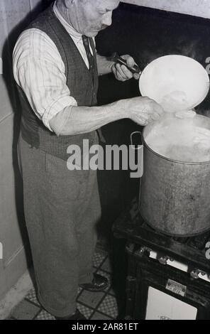 Années 1950, historique, faire de l'hydromel, un homme âgé réchauffant des épices dans un récipient en métal dans le processus de fabrication de la boisson alcoolisée hydromel, également connu sous le nom de vin de miel, Angleterre, Royaume-Uni. Une ancienne boisson fabriquée pour la première fois lorsque la fermentation des aliments a été découverte. Banque D'Images