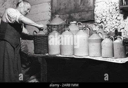 Années 1950, historique, Making mead, un homme dans son sous-sol mettant le bouchon sur une bouteille en grès de sa maison Made mead, une ancienne boisson alcoolisée, également connue sous le nom de vin de miel, Angleterre, Royaume-Uni. Fabriqué en fermentant du miel avec de l'eau, et parfois des fruits, des épices, des céréales ou du houblon, l'hydromel aurait été découvert à un moment donné au Néolithique avec l'introduction de la fermentation alimentaire. Banque D'Images