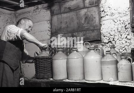 Années 1950, historique, Making mead, un homme dans son sous-sol mettant le bouchon sur une bouteille en grès de sa maison Made mead, une ancienne boisson alcoolisée, également connue sous le nom de vin de miel, Angleterre, Royaume-Uni. Fabriqué en fermentant du miel avec de l'eau, et parfois des fruits, des épices, des céréales ou du houblon, l'hydromel aurait été découvert à un moment donné au Néolithique avec l'introduction de la fermentation alimentaire. Banque D'Images