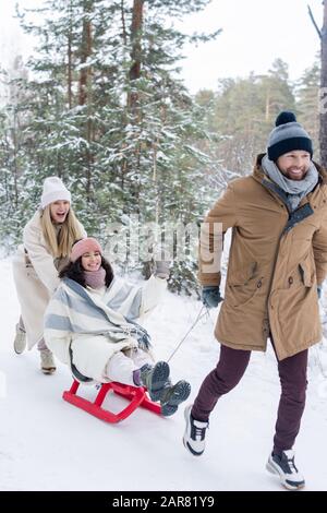 Un jeune homme heureux en hiver, qui tire des traîneaux avec une jeune fille gaie dans le parc Banque D'Images