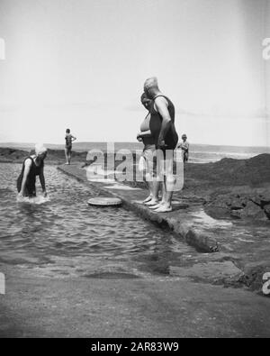 Années 1930, bains historiques, hommes et femmes adultes dans les costumes de natation de l'époque dans une piscine de mer sur la côte, Bideford, Devon, Angleterre, Royaume-Uni. La nage en plein air en plein air ou les bassins de pagayage en partie construits par des rochers ont été un élément visible dans les zones côtières de Devon et de Cornwall. Banque D'Images