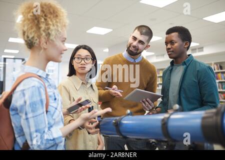 Groupe multi-ethnique d'étudiants discutant de projet et gestuant activement tout en se tenant à la bibliothèque de collège Banque D'Images