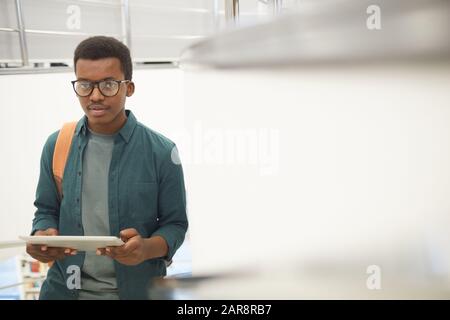 Taille vers le haut portrait de jeune homme africain tenant une tablette numérique et regardant l'appareil photo tout en se tenant sur l'escalier à l'université, espace de copie Banque D'Images