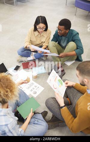 Vue en grand angle sur un groupe multi-ethnique d'étudiants assis au sol tout en travaillant sur un projet à la bibliothèque de l'université, espace de copie Banque D'Images