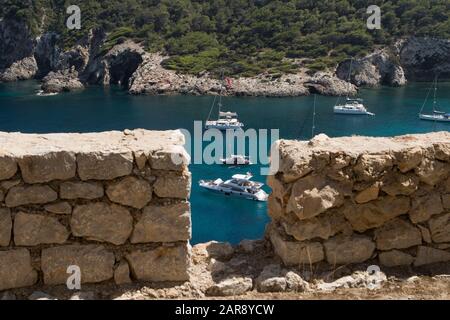 Vue depuis un mur de pierre donnant sur la baie de Cala Llonga et les bateaux sur l'eau bleu cristal à Cala Llonga, Ibiza, les îles Baléares Banque D'Images