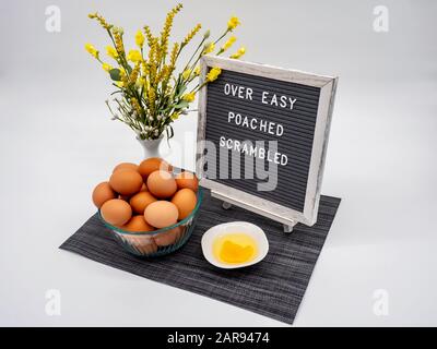 Lettre Board avec un bol D'Œufs bruns, un oeuf Fissuré dans un bol, des fleurs jaunes et Des Mots Épelés, Sur Facile, poché, Brouillé. Banque D'Images