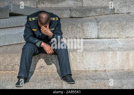Le triste policier est assis sur la parole avec son avait baissé, il a perdu son emploi, il est seul. L'homme porte des rayures. Était en panne. Pleurs mâles dans les escaliers. Banque D'Images