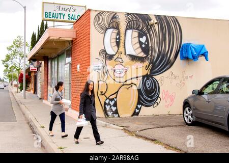 Les piétons hispaniques marchent devant un parking de Santa Ana, Californie, salon de beauté décoré d'une fresque humoristique représentant leur client idéal. Banque D'Images