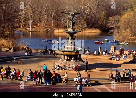 Les piétons multiraciaux se détendent autour de la fontaine de Bethesda dans Central Park, New York City. La fontaine a été conçue par Emma Stebbeins en 1868. Elle a été la première femme à recevoir une commission publique pour une œuvre d'art importante à New York. La statue en bronze de huit pieds représente un ange ailé féminin qui touche le haut de la fontaine. Sous elle se trouvent quatre chérubins de quatre pieds représentant la tempérance, La Pureté, la santé et la paix Banque D'Images