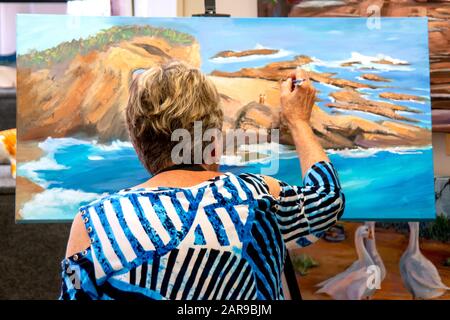 Une femme artiste senior met les touches de finition sur sa peinture d'un rivage rocheux à Laguna Beach, CA. Banque D'Images