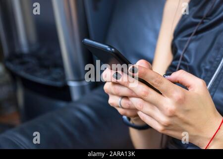 Une fille en cuir avec des ongles noirs se trouve sur un canapé en cuir et tient un téléphone dans ses mains. Mise au point sélective Banque D'Images