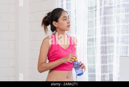 La jeune femme asiatique prend un repos après l'entraînement et boire de l'eau après l'entraînement dans le salon Banque D'Images