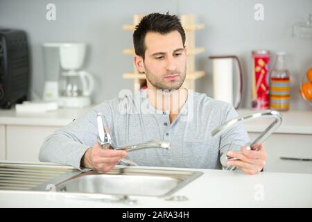 un jeune homme agréable et heureux qui fixe le robinet dans la cuisine Banque D'Images