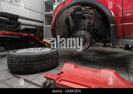 Véhicule d'occasion rouge avec capot ouvert relevé sur un pont élévateur pour la réparation du châssis et du moteur avec roues déposées et pare-chocs cassé dans un atelier de réparation de véhicule. A Banque D'Images