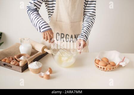 Les mains du jeune homme fouetter les œufs avec le sucre pour faire cuire un gâteau aux fruits. Pâte à tarte cuisson mâle sur le tableau blanc Banque D'Images