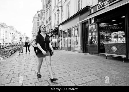 Fille portant des écouteurs marchant sur le pavé, rue Saint Antoine, Paris, France, Europe Banque D'Images