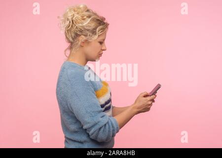 Vue latérale d'une jolie femme sérieuse avec des cheveux courts en sueur chaud chat dans le téléphone portable, lire le message, en utilisant le téléphone portable avec un look attentif Banque D'Images