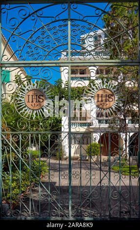 Le Christogram IHS sur une porte élaborée en fer forgé menant à l’arrière-cour de l’église Saint-Augustin. Macao, Chine. Banque D'Images