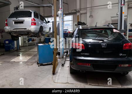 Novosibirsk, Russie - 08.01.2018: Deux voitures d'occasion Acura MDX et Luxgen soulevées sur un ascenseur pour réparer le châssis et le moteur dans un atelier de réparation de véhicules. A Banque D'Images