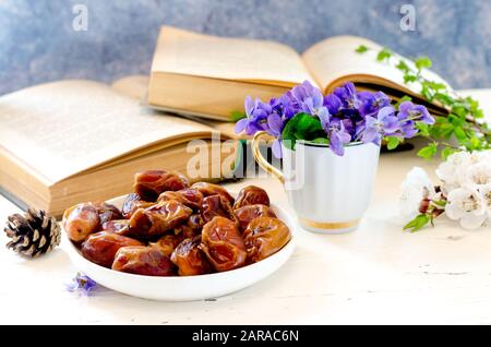 Bol avec des fruits secs sucrés de dattes dans une composition avec des fleurs violettes et des livres d'époque. Ramadan, cuisine traditionnelle. Banque D'Images