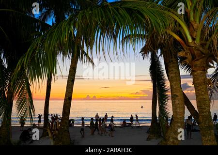 Île de Boracay, province d'Aklan, Philippines : les gens de la plage blanche profitent du coucher du soleil. Palmiers encadrant l'image. Banque D'Images