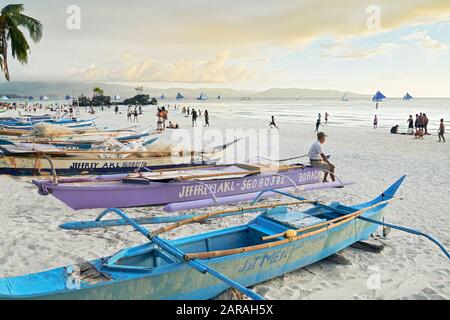 Île de Boracay, province d'Aklan, Philippines - 1 janvier 2020: Vieil homme assis sur un bateau de pêche, regardant les gens et coucher de soleil à la plage blanche Banque D'Images