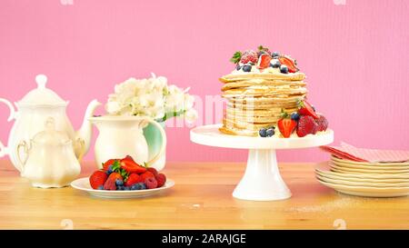 Shrove Pancake Mardi, dernier jour avant Carême, pile de crêpes gâteau préparé avec des couches de crème fouettée et des baies fraîches contre le dos rose moderne Banque D'Images