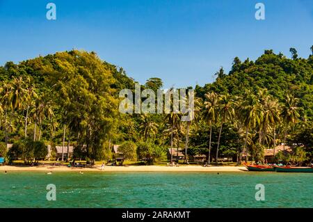 Vue sur l'île de Rabbit, Cambodge de la mer avec des bateaux mordés sur la plage et des touristes étrangers nageant au large de la plage de sable bordée de palmiers. Banque D'Images