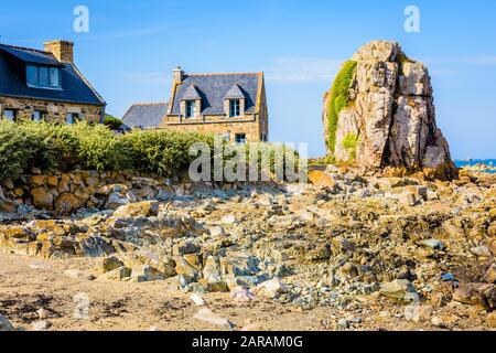 Maisons typiques en granit avec toit en ardoise dans le petit port de Pors Hir en Bretagne, construites sur le bord de mer à côté d'un bloc, par une journée d'été ensoleillée. Banque D'Images