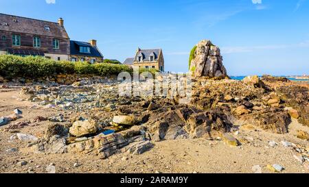 Maisons typiques en granit avec toit en ardoise dans le petit port de Pors Hir en Bretagne, construites sur le bord de mer à côté d'un bloc, par une journée d'été ensoleillée. Banque D'Images