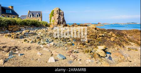 Maisons typiques en granit avec toit en ardoise dans le petit port de Pors Hir en Bretagne, construites sur le bord de mer à côté d'un bloc, par une journée d'été ensoleillée. Banque D'Images