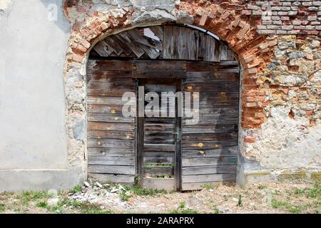 L'entrée de l'arrière-cour de la maison familiale de banlieue abandonnée est fermée avec des panneaux en bois fissurés et de petites portes délabrées à l'intérieur d'un cadre décoratif en rouge Banque D'Images