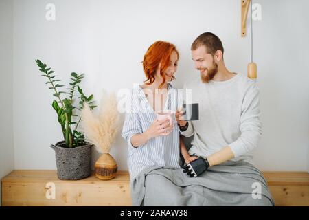 Heureux mari et femme assis ensemble sur une étagère, boire du café à la maison. Banque D'Images