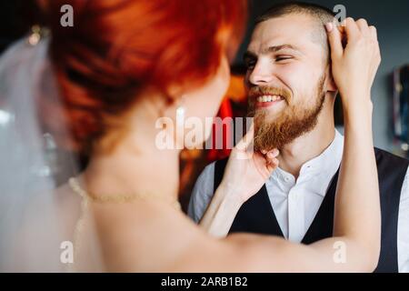 Mariée toilettant son futur mari dans une salle lumineuse avant la cérémonie de mariage Banque D'Images