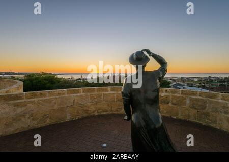 Statue en bronze d'une femme, en soirée, tenant son chapeau dans la brise de la mer surplombant le port de Geraldton sur le site commémoratif du HMAS Sydney 11. Banque D'Images