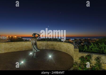 Statue en bronze d'une femme, en soirée, tenant son chapeau dans la brise de la mer surplombant le port de Geraldton sur le site commémoratif du HMAS Sydney 11. Banque D'Images