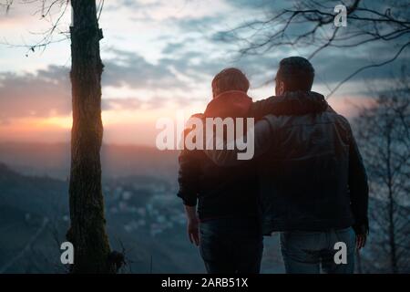 Vue arrière des amis regardant le coucher de soleil sur la falaise avec la ville Banque D'Images