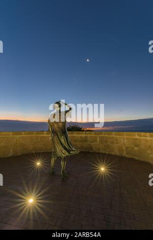 Statue en bronze d'une femme, en soirée, tenant son chapeau dans la brise de la mer surplombant le port de Geraldton sur le site commémoratif du HMAS Sydney 11. Banque D'Images