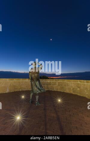 Statue en bronze d'une femme, en soirée, tenant son chapeau dans la brise de la mer surplombant le port de Geraldton sur le site commémoratif du HMAS Sydney 11. Banque D'Images